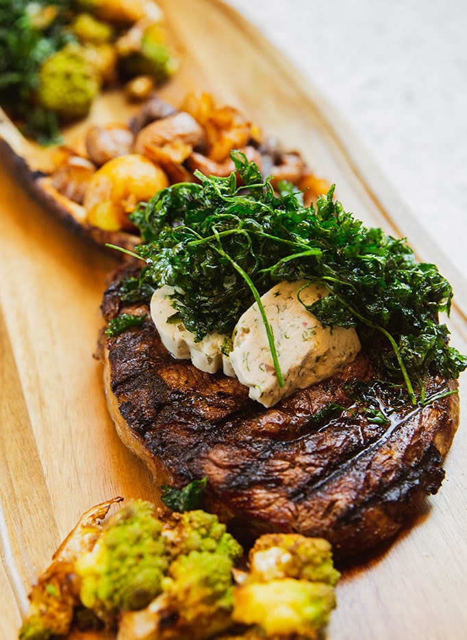 Photo of the 28oz Prime Tomahawk Ribeye served with Truffle Crushed Potato, an Herb Butter, Roasted Wild Mushrooms, and Romanesco